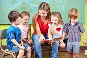 Kinder mit Erzieher lesen Buch im Kindergarten